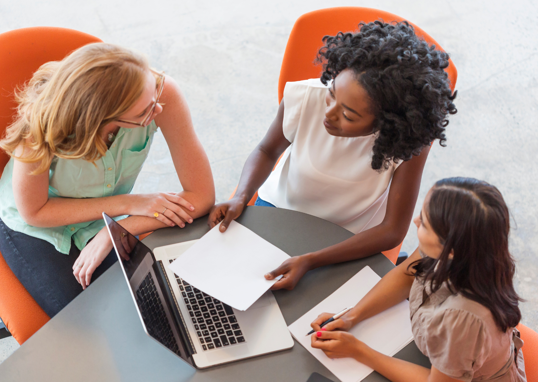 Three women discussing something at a table with a computer and documents
